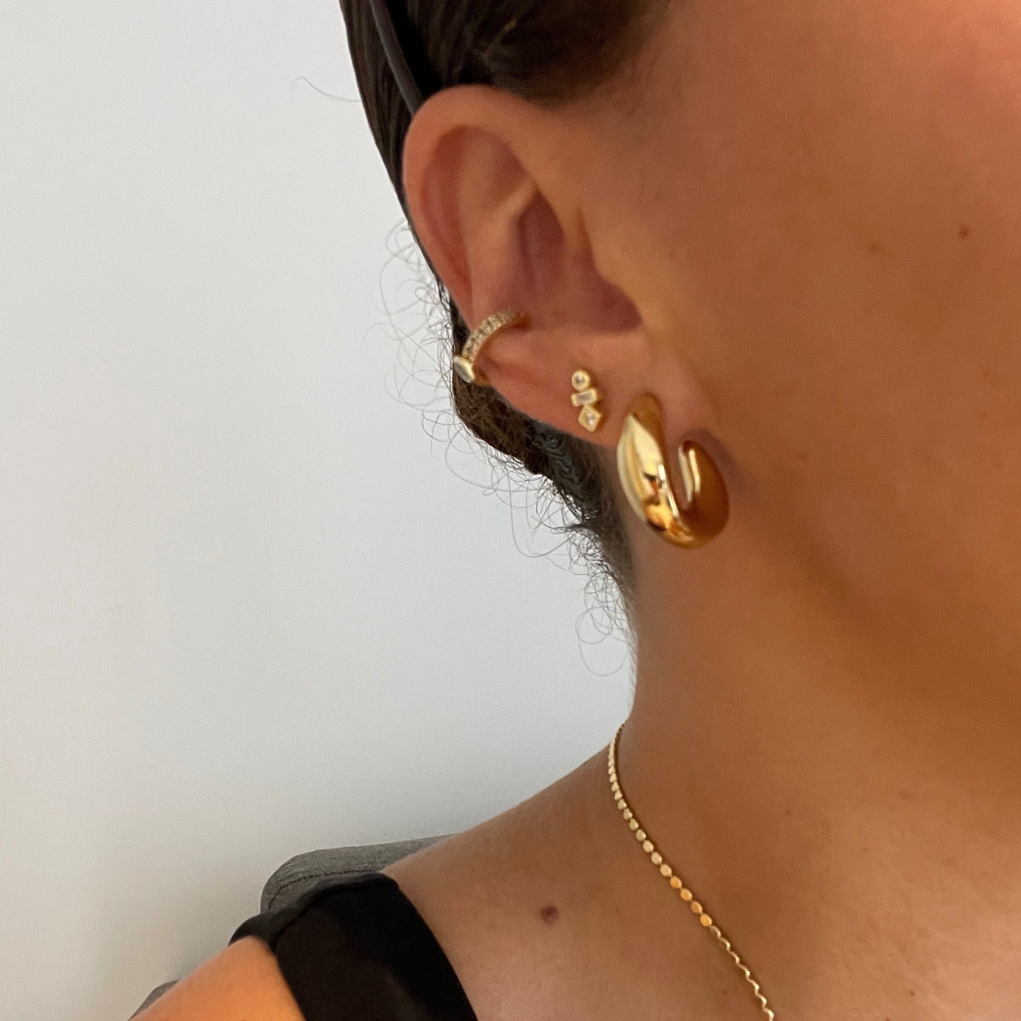 Close-up of a person wearing gold hoop earrings and a necklace against a plain background