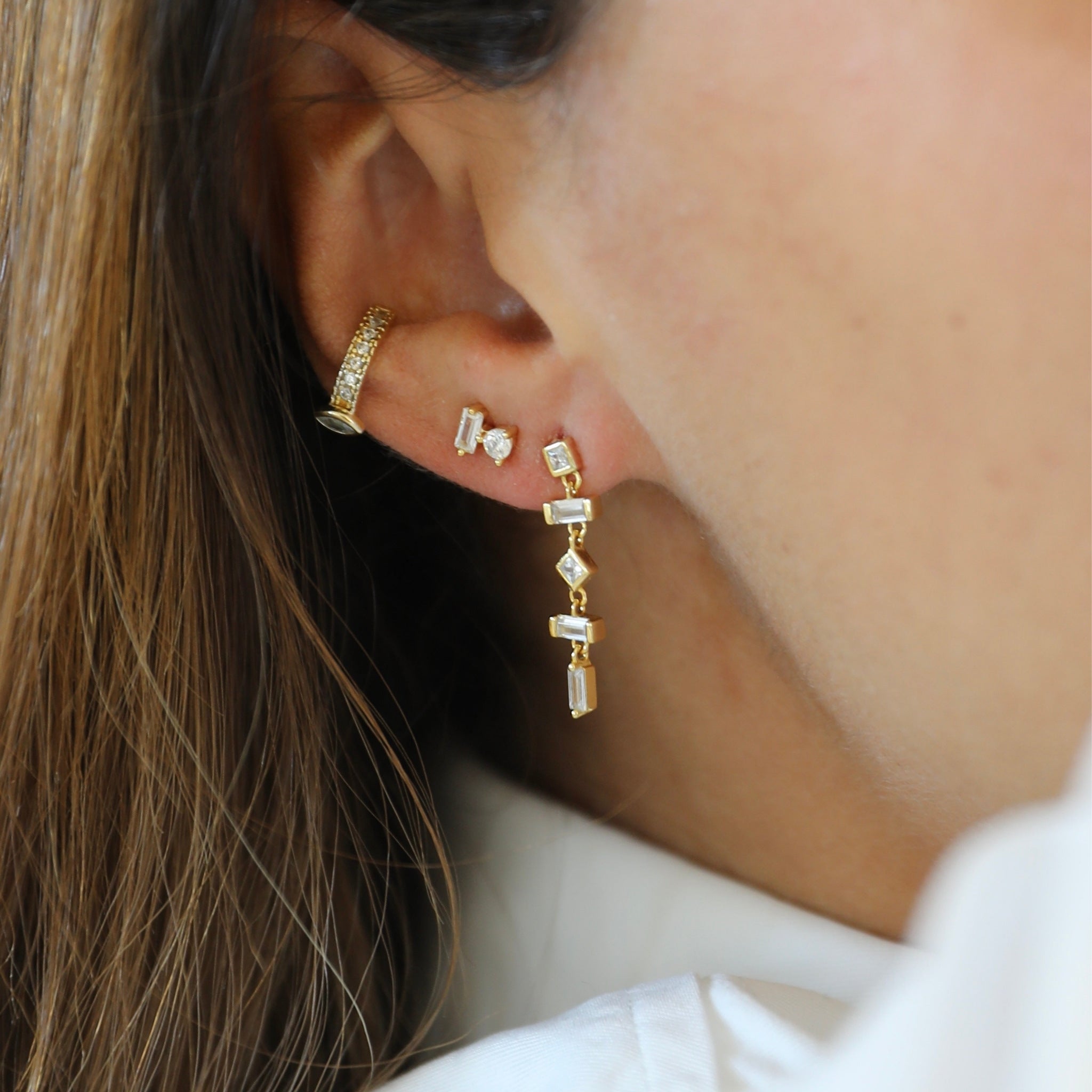 Close-up of an ear wearing gold hoop earrings and dangling diamond earrings. Ear stack