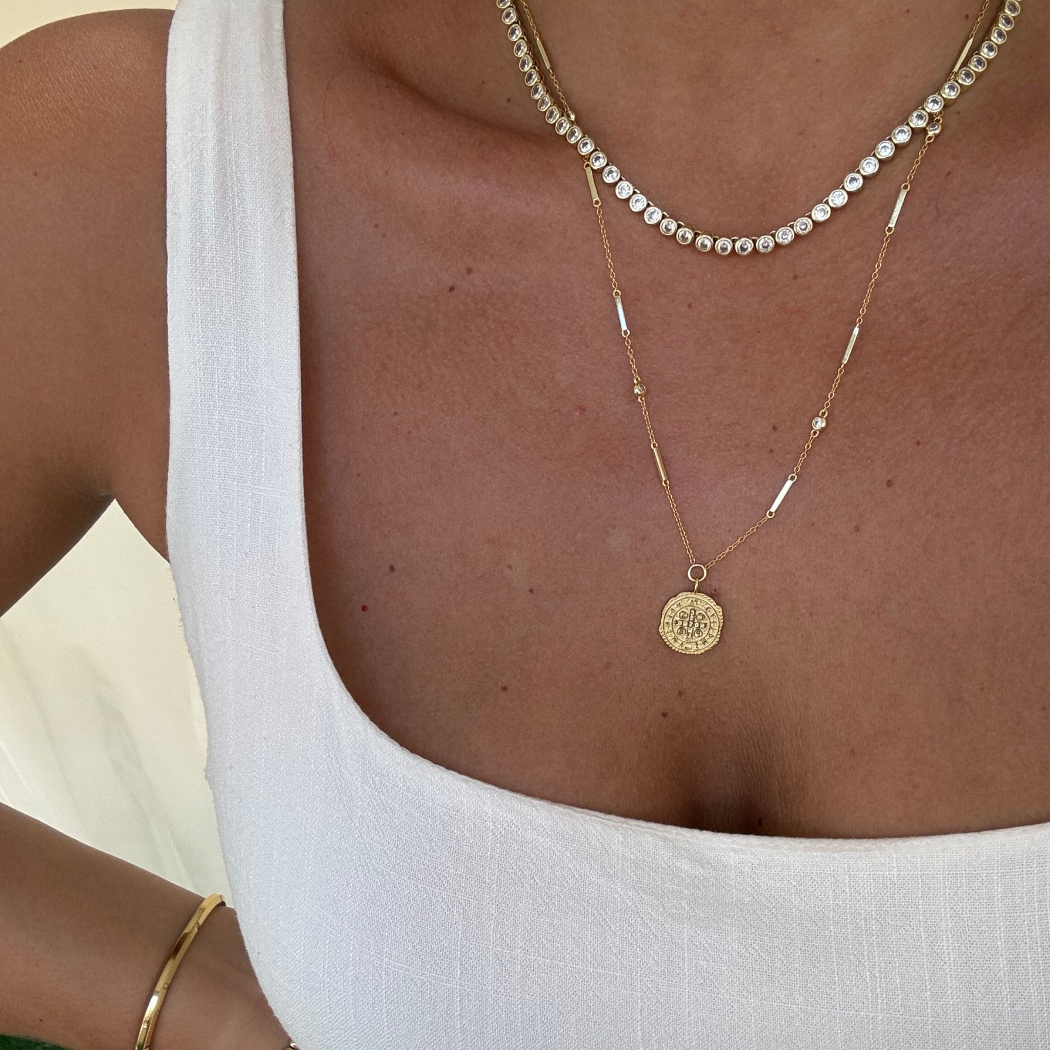 Gold coin necklace layered with CZ tennis necklace on model in white top – Nikki E. Designs